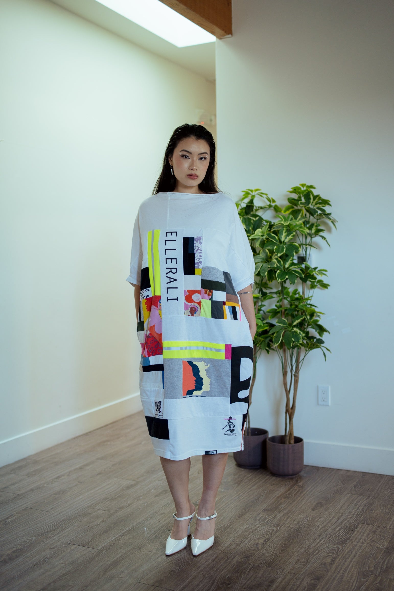 Woman wearing a colorful dress with geometric patterns in a room with a plant and light fixture.